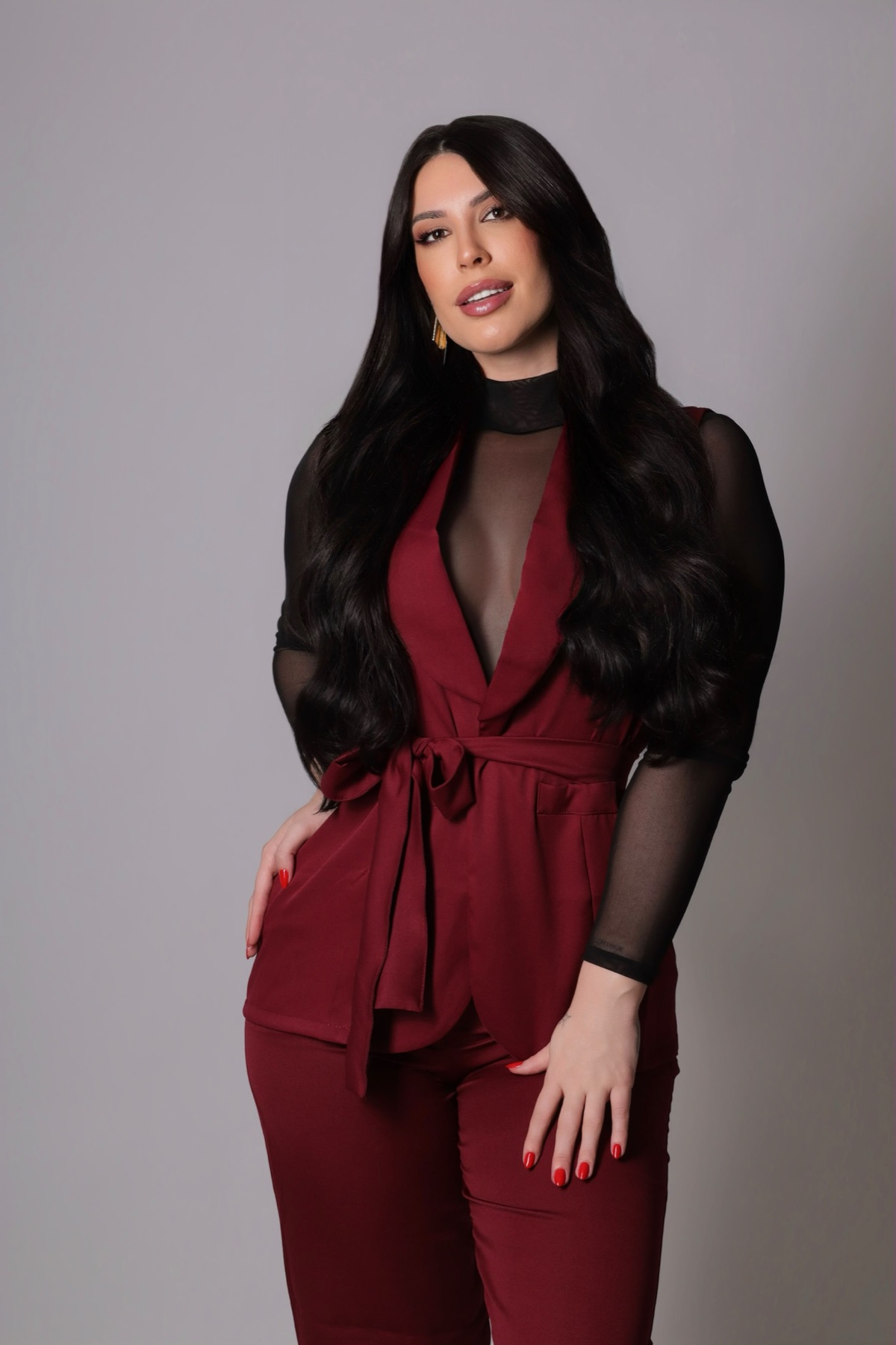 Mulher de conjunto vinho e blusa de tule, sorrindo para a câmera